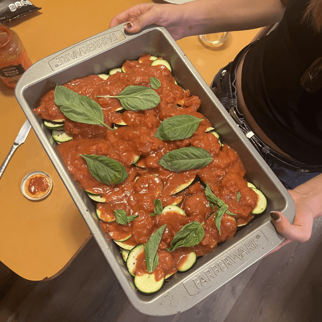 A pan full of sliced vegetables, topped with vodka sauce and basil.